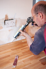 Kitchen Fitters: Sealing the Worktop. A worker applying sealant to fill and make a worktop waterproof. From a series of related images.