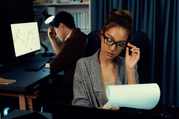 Businesswoman with stressful face looking document paperwork file while coworker trading stock...