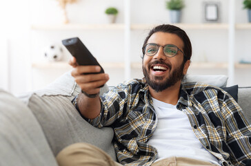 Relaxed arab guy wathcing movie on TV at home, sitting on couch alone, having happy face...