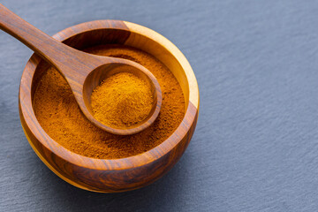 Turmeric roots and powder in a wooden bowl on a dark slate board: natural superfood and culinary spice