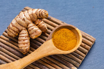 Turmeric roots and powder in a wooden bowl on a dark slate board: natural superfood and culinary spice