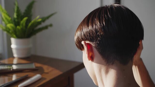 Young woman styling trendy undercut hairstyle, natural sunlight illuminating her from nearby window, showcasing confident personal grooming technique