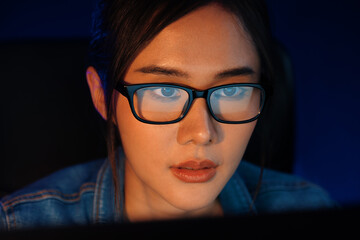 Fototapeta premium Portrait young beautiful Asian creative with glasses of serious face looking on pc to search project creator social media online, planning strategy creator at neon modern office at night. Stratagem.