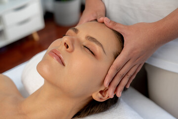 Caucasian woman enjoying relaxing anti-stress head massage and pampering facial beauty skin recreation leisure in dayspa modern light ambient at luxury resort or hotel spa salon. Quiescent