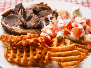 Dinner meal with cooked lamb loin chops, potato lattice and fresh salad with sour cream. Close up. Fine tasty dinner.