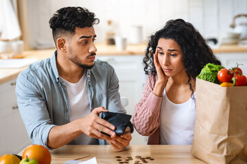 Coronacriris Concept. Depressed Arab Couple In Kitchen Counting Remaining Money After Food Shopping, Upset Middle Eastern Spouses Looking At Empty Wallet, Shocked By Big Prices For Grocery, Closeup