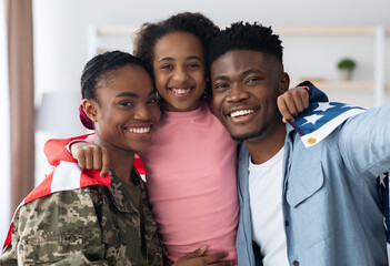 Positive black family father, daughter and mother soldier posing with flag of the US, african american woman in military uniform return home from army, celebrating reunion with husband and kid
