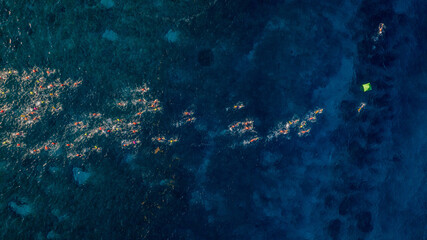 Nadadores en mar cristalino rodeando boya naranja durante competencia de aguas abiertas.