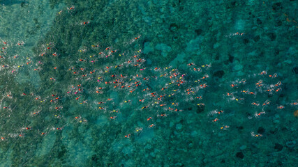 Nadadores en mar cristalino rodeando boya naranja durante competencia de aguas abiertas.