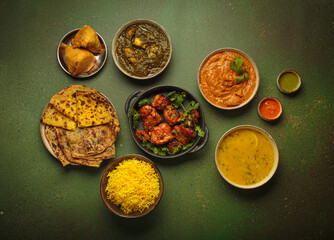 Overhead view of a variety of Indian dishes on a green table, including curry, tandoori chicken,...
