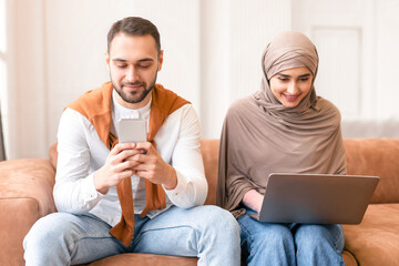 Gadget Lifestyle. Modern Muslim Couple Using Laptop And Smartphone Spending Time Together...