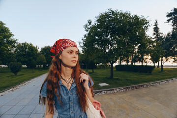 Lifestyle woman in modern boho-western denim street style wearing a red bandana, walking outdoors during golden hour with natural greenery and warm film color tones.