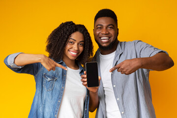 New mobile app. Cheerful african american couple holding and pointing at smartphone with black...