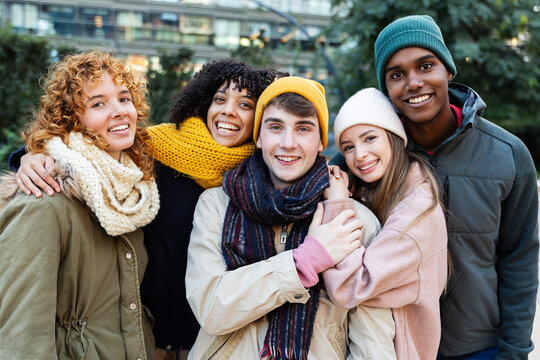 Young happy group of diverse friends in warm clothes smiling at camera standing together outside. Portrait of millennial people enjoying winter vacation. Friendship and youth concept.