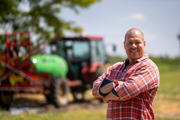 Smiling male farmer stands in front of tractor on sunny day