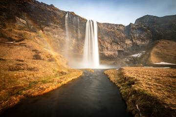 Long exposure of scenic view of Seljalandsfoss waterfall with river and golden grassland in southern Iceland on a sunny spring day