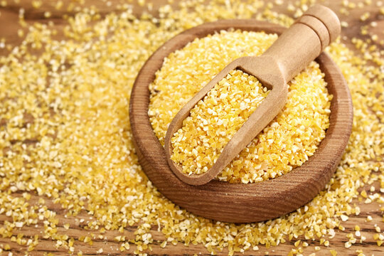 Spoon of coarse semolina on rustic wooden background, gluten free yellow corn grain for healthy diet, selective focus, shallow DOF