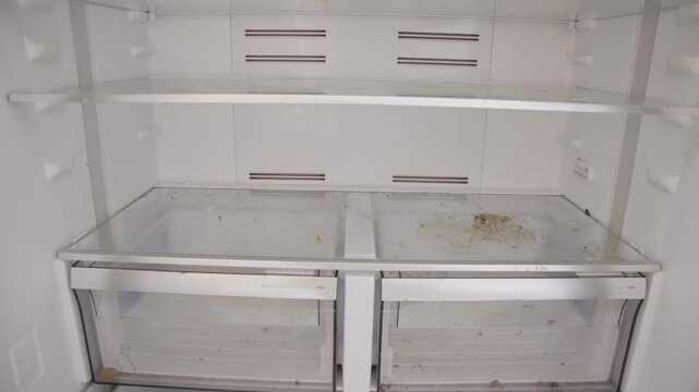 Empty refrigerator with no food inside and open doors in house or apartment. Poor family in low income conditions nothing in fridge or freezer. Drawers without groceries and food items