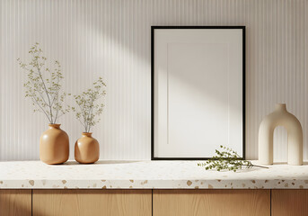 Stylish interior scene featuring two terracotta vases with greenery, a sculptural white vase, and an empty black-framed picture on a stone surface.