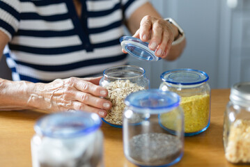 Senior woman using glass jars to store food at home kitchen


