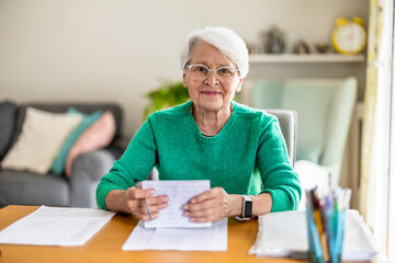 Senior woman sitting in the living room and doing paperwork

