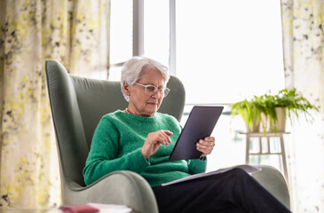 Senior woman using digital tablet while sitting in armchair at home
