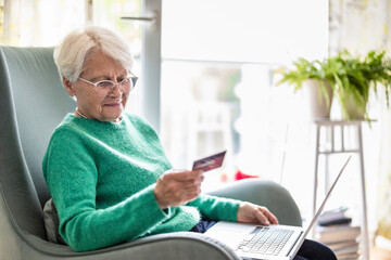Senior woman using laptop and credit card for online shopping at home

