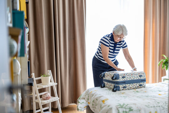 Senior woman packing a suitcase for travel on a bed at home
 - Powered by Adobe