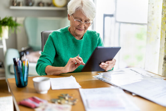 Senior woman using a tablet while organizing household paperwork in the living room