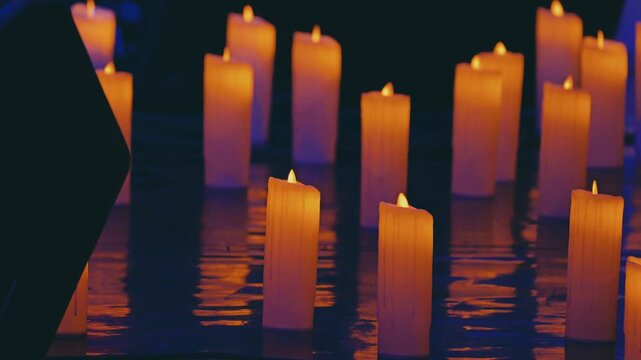 A collection of lit candles on a reflective surface, casting a warm glow. The soft, subdued lighting creates a tranquil and serene atmosphere, enhancing the peaceful mood