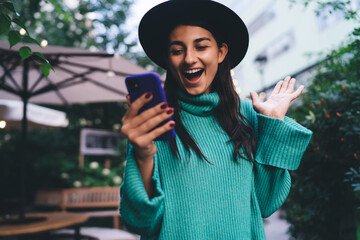 Young woman laughs with phone in hand, reacting to digital content with joy, illustrating...