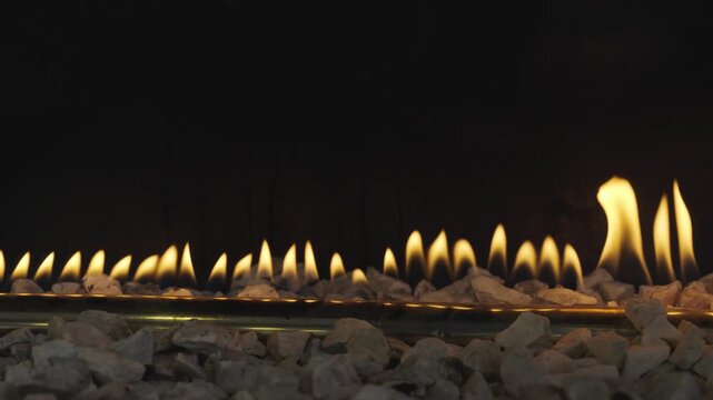 Yellow flames rise in a linear pattern from a gas fireplace with white stones, creating a cozy and modern ambiance.