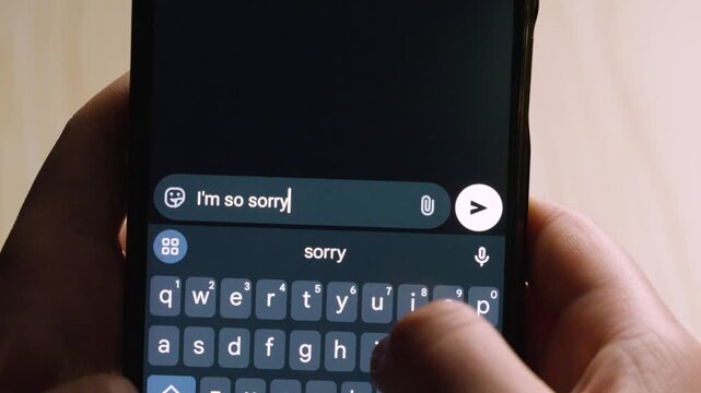 Close-up of hands holding a smartphone while composing and preparing to send the message "I'm so sorry."