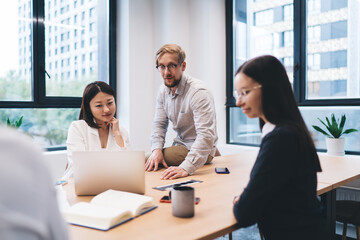 Startup team meeting in bright coworking space, engaged in focused discussion around laptop and printed documents, planning next steps with shared strategy and modern technology.