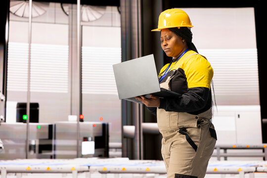 Professional engineer uses digital interface to supervise automated factory. The industry 4.0 system, features robotic arms and assembly lines, drives efficiency across modern industrial production.