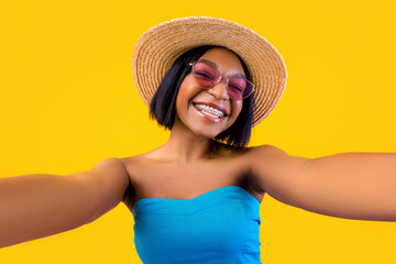 Portrait of joyful African American woman in summer outfit taking selfie on mobile phone over...