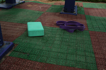 Gym equipment objects in outdoor urban street sport ground with safe rubber surface green red colors. Dumbbell, pilates ring, yoga block, fitness band lying on the floor with no people
