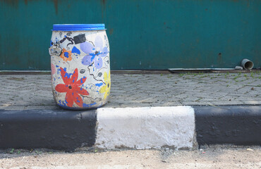 used barrel with a picture painted on it is displayed on the side of the road as a place to dispose of rubbish, unique and creative