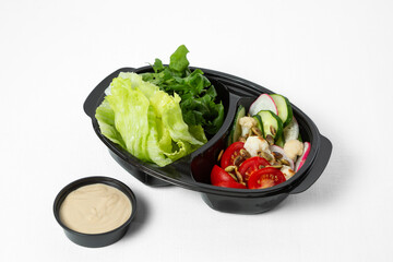 Fresh chopped vegetables for salad in a bowl with sauce on a white background