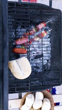 Chilean Independence Day vertical video: Overhead close-up of woman placing anticuchos on grill with marraquetas and longanizas during festive celebration