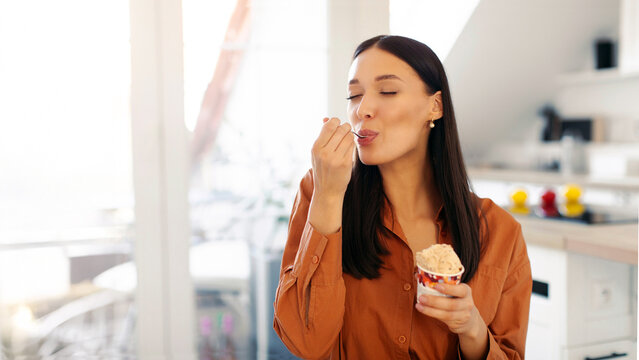 Satisfied woman eating delicious ice cream with closed eyes, licking spoon, enjoying frozen dessert in hot weather, copy space