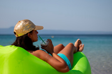 Portrait of a cute woman drinking cold chocolate and lying on an inflatable mattress on a summer beach. A girl having fun on the beach on summer vacation.