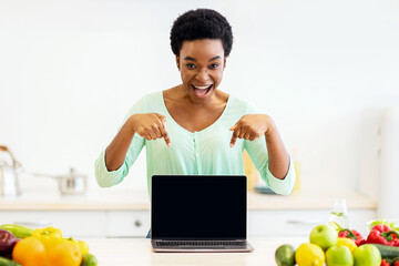 Excited African Woman Pointing Fingers At Laptop With Blank Screen Advertising Cooking Cources...
