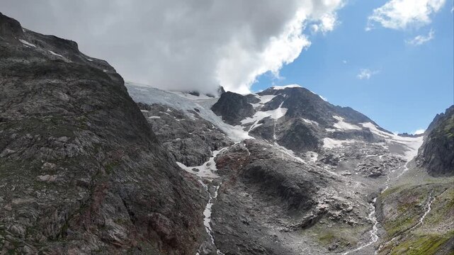 panorama on glacial ice and mountain cliff, slow motion movement upwards toward glacier, cloud touching Steingletscher, Switzerland, drone shot