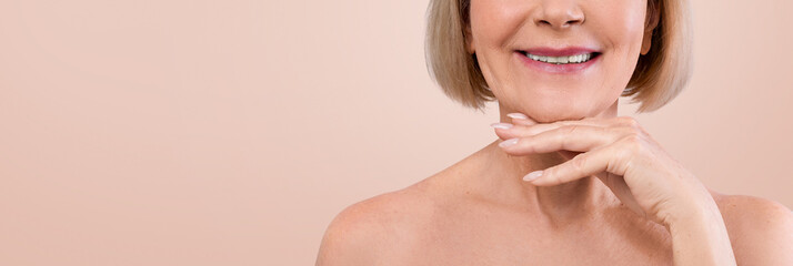 Cropped of smiling senior woman touching her chin, posing half-naked over beige studio background,...