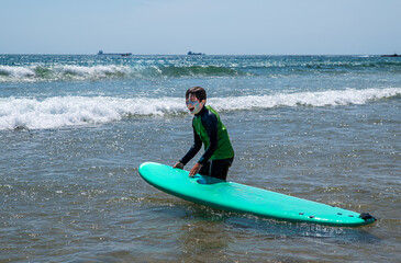 Excited 9-year-old boy in a wetsuit learning to surf with a surfboard in waves. 