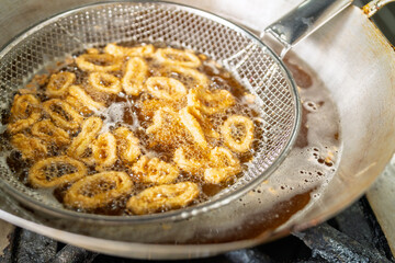 Chef frying calamari rings in boiling oil using metal strainer