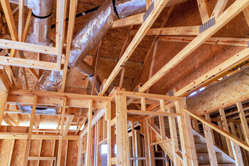 Wooden framing, ventilation ducts expose progress of residential building during works daytime.