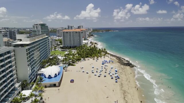 Drone, facing west, lowers on Atlantic Beach on sunny morning in San Juan, Puerto Rico