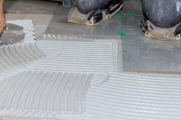 Construction workers apply adhesive on floor for tile installation in bright work area.
